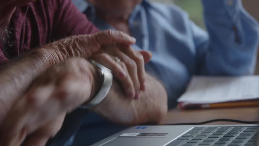 A man and woman hold hands by the laptop