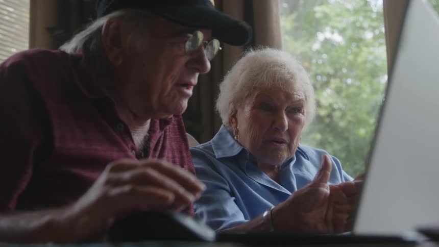 Laptop on a table with two elderly people sitting around talking