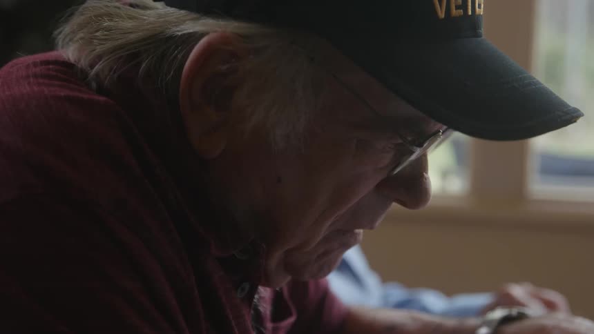 Elderly man sitting next to another person looking at documents at a table