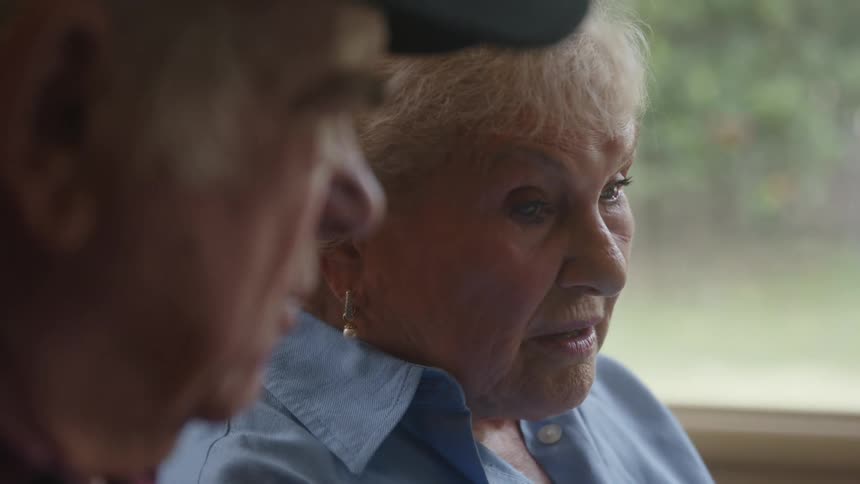 Elderly woman sitting looking at a document next to a man