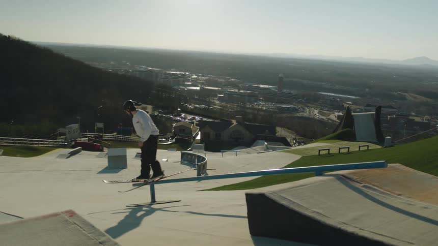 A man with skis jumps on a metal pipe and slides down onto concrete