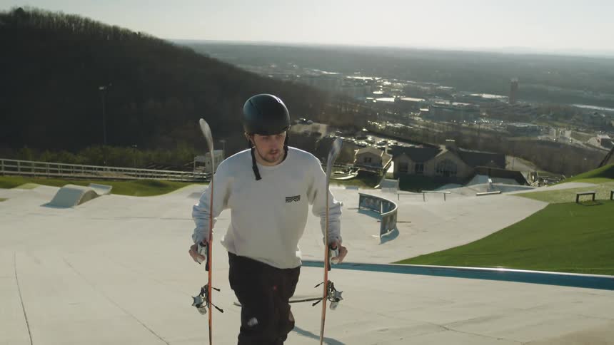 Man carrying skis and poles walking towards a jumping ramp