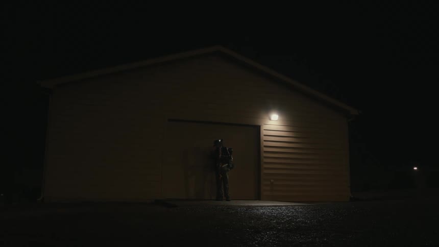 A person holding snowboards is leaving a garage and closing the door