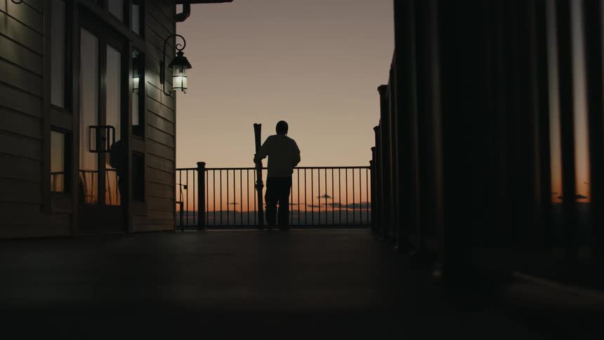 A person with his back is walking towards a metal railing to observe the landscape