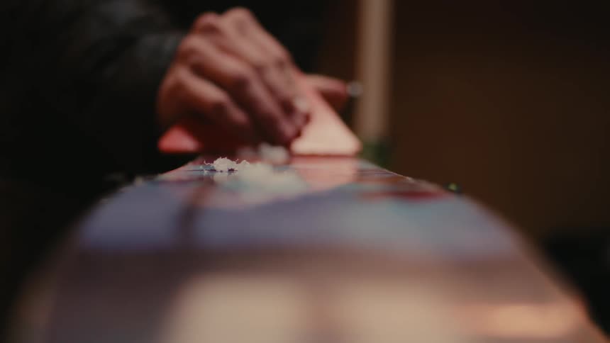 A person using a triangular tool is scraping the surface of a wood