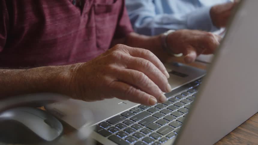 Pair of hands of an elderly person typing on a laptop