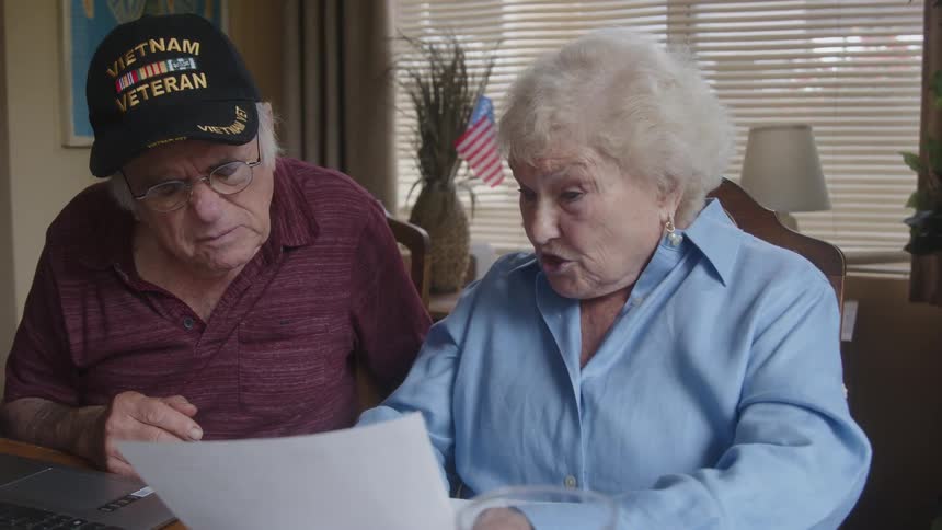 Man and an elderly woman sitting at a table reading a document and talking