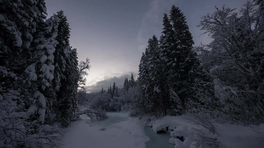 Dark clouds move over a forest and river covered in snow