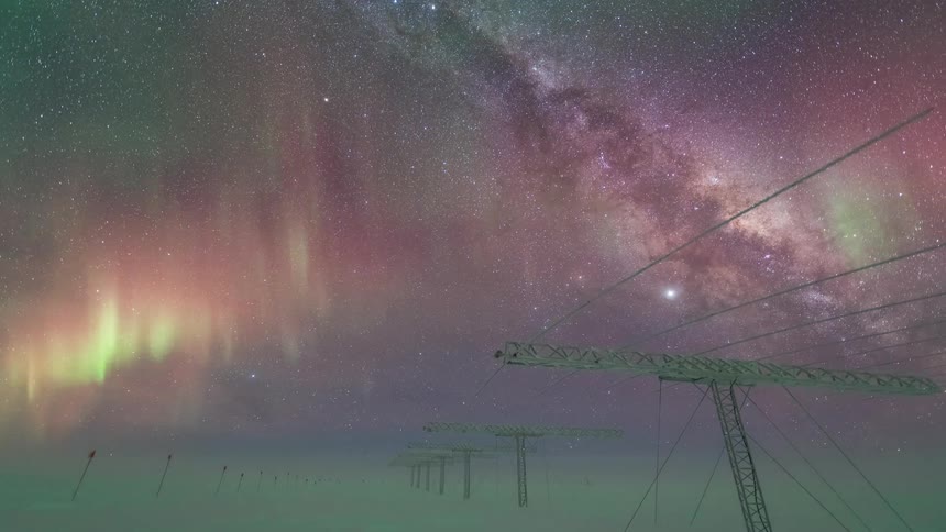 Aurora borealis with shades of green and pink illuminating the starry night sky above a snowcovered landscape with some polar research structures