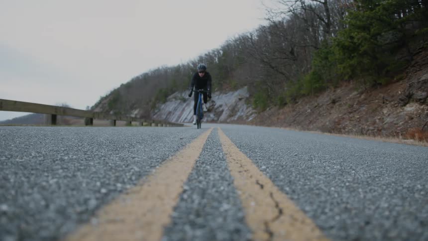 A man rides a bicycle on a remote road near a forest
