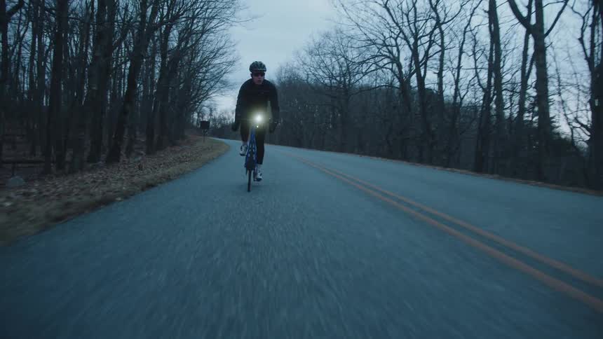 Cyclist man pedaling along a paved street surrounded by trees