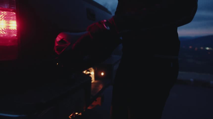 A young man takes a bicycle helmet out of the back of a pickup truck parked in the countryside a dusk