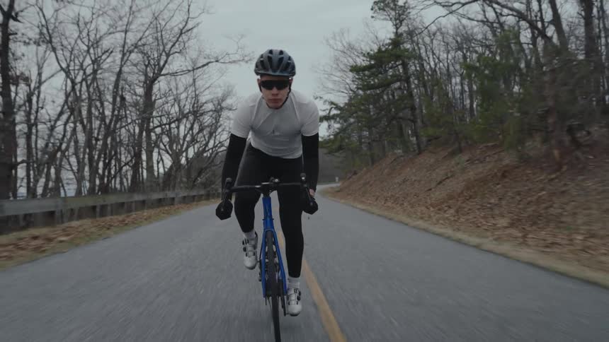 A bike rider travels down a remote road running through a forest