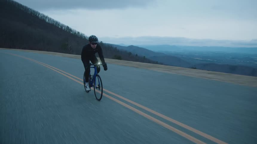 A man is cycling on a two lane highway on a cloudy day