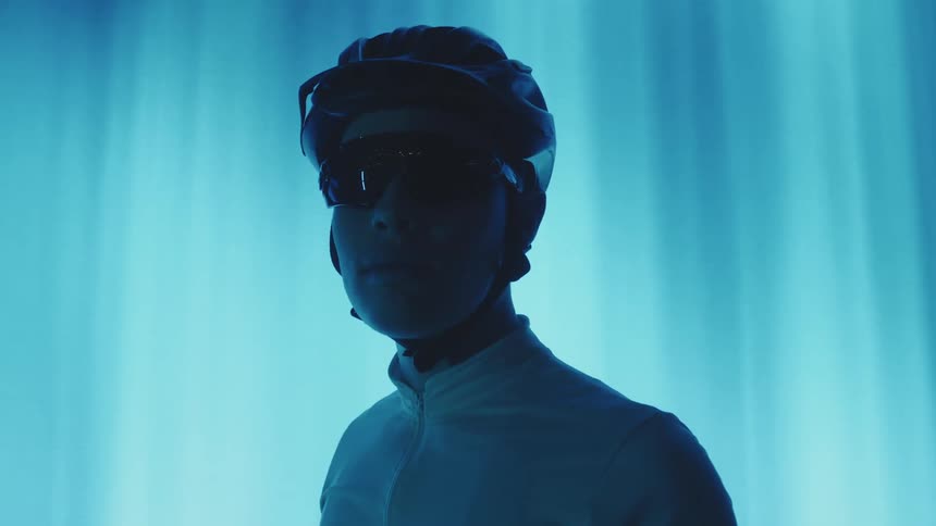 A man wearing sunglasses and a bike helmet stands in front of a large lighted screen