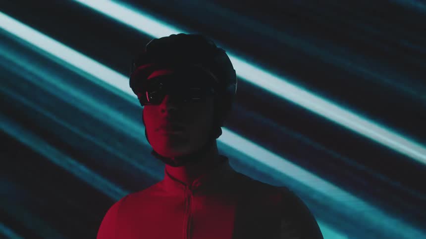 A silhouette of a person wearing sunglasses and a bicycle helmet against a backdrop of moving diagonal blue light stripes