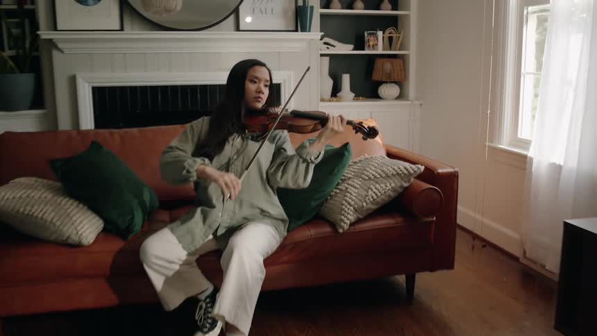 Young woman sitting in the living room playing the violin