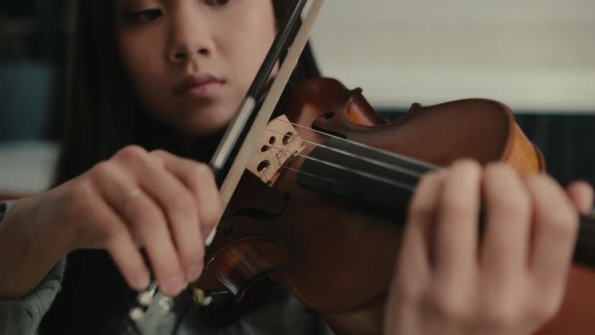 A closeup of a young woman playing violin in a room