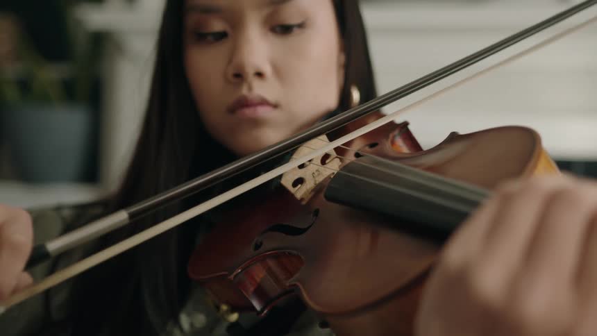 An asian woman focuses as she plays a piece on a violin