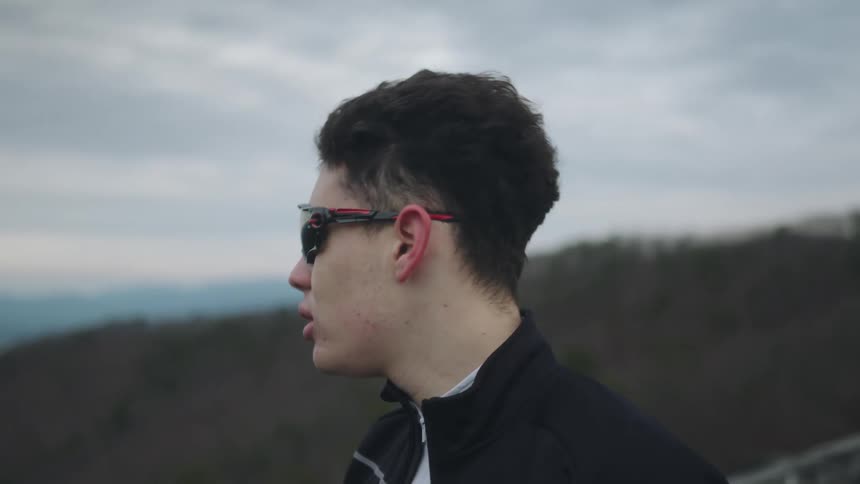 Man with sunglasses taking a deep breath while standing outdoors on a cloudy day