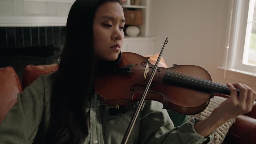 A woman plays the violin while sitting on a couch