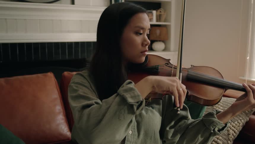 An asian woman plays a violin in a living room