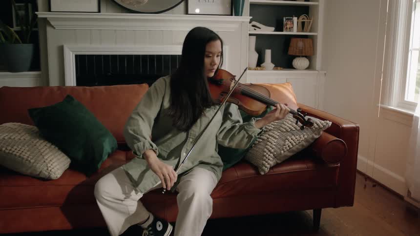 As asian woman sitting on a couch plays a violin