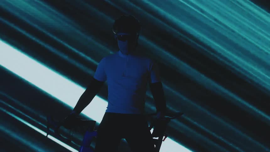 Silhouette of a cyclist with a helmet and glasses next to a bicycle against the background of a screen with lights passing by