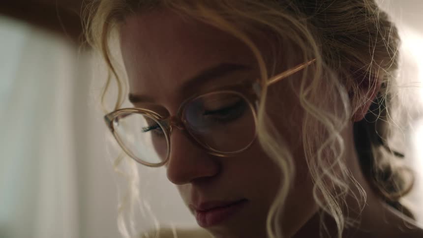 Close up of a beautiful blonde woman with long hair and glasses painting with a brush