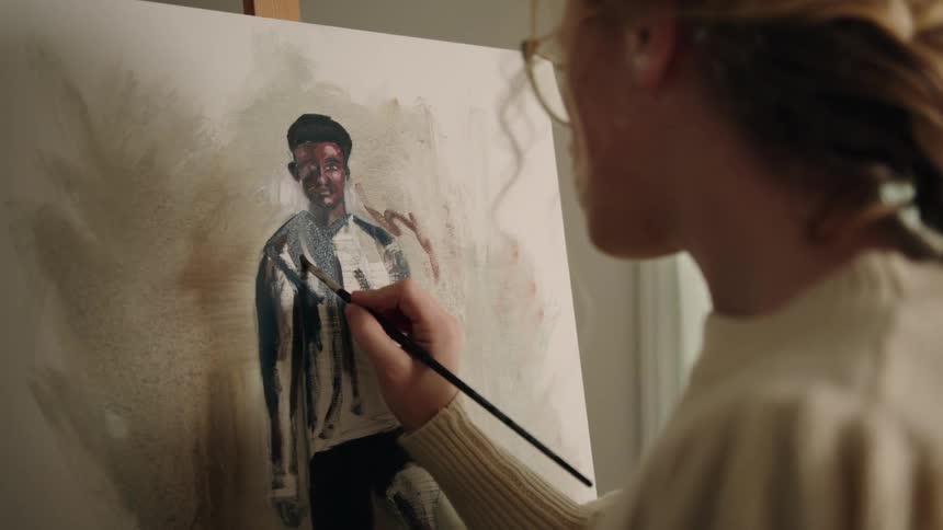 An artist applying brushstrokes to a painting of a young man oil painting over a large canvas