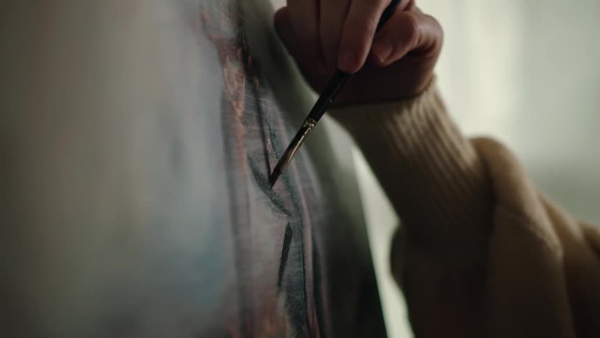 Closeup of an adult hand painting on a canvas