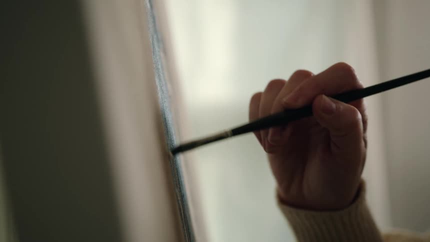 A woman applies brushstrokes to a canvas in a room