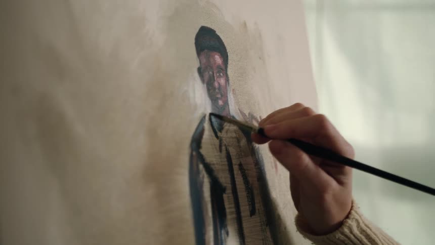 An adult hand paints the clothing of a black man on a canvas