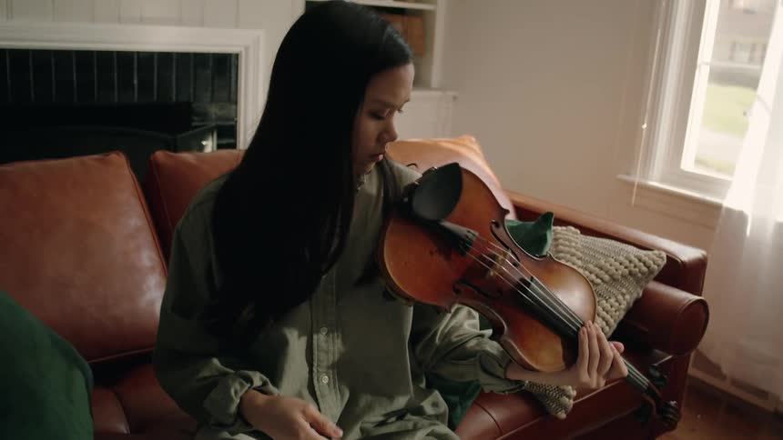 Young woman sitting on a leather sofa preparing a violin to play