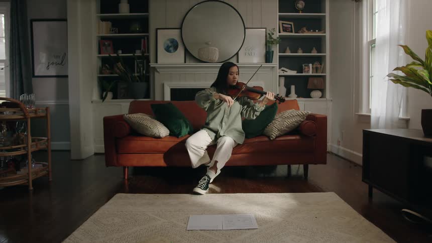 An asian woman plays a violin with sheet music on a rug in front of her