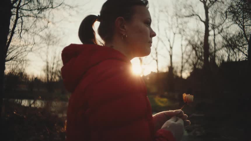 A woman is holding a flower by the stream