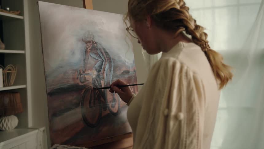 A woman carefully applies brushstrokes to a painting of a person riding a bicycle
