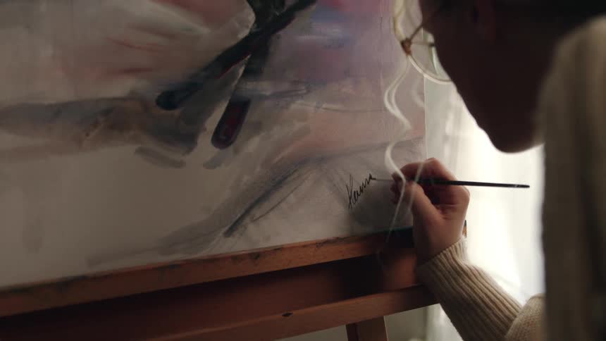 A painter person is writing his signature on a painted art board