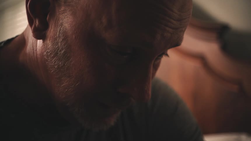 A very sad man looks to be grieving while sitting in a bedroom