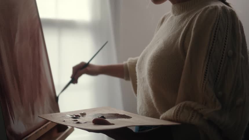 A woman applies brushstrokes to a painting sitting on an easel