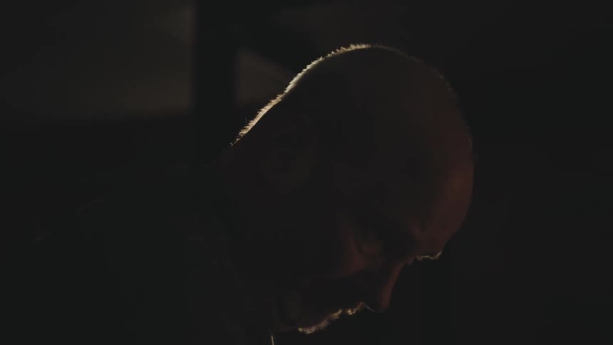 A bald man punches a bag inside of a dark room
