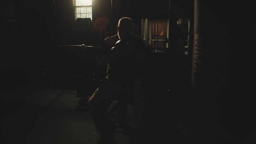 A bald man ties up a boxing glove in a dark room