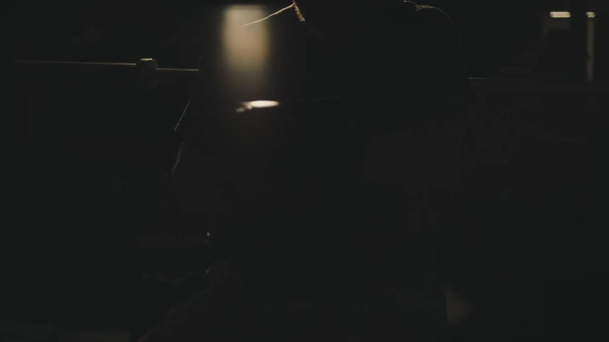 Silhouette of a man adjusting boxing gloves in a dimly lit room