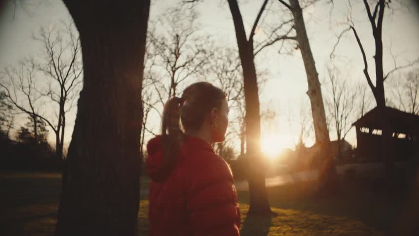 Woman walking in a field with trees and the reflection of sunset sunlight on the horizon