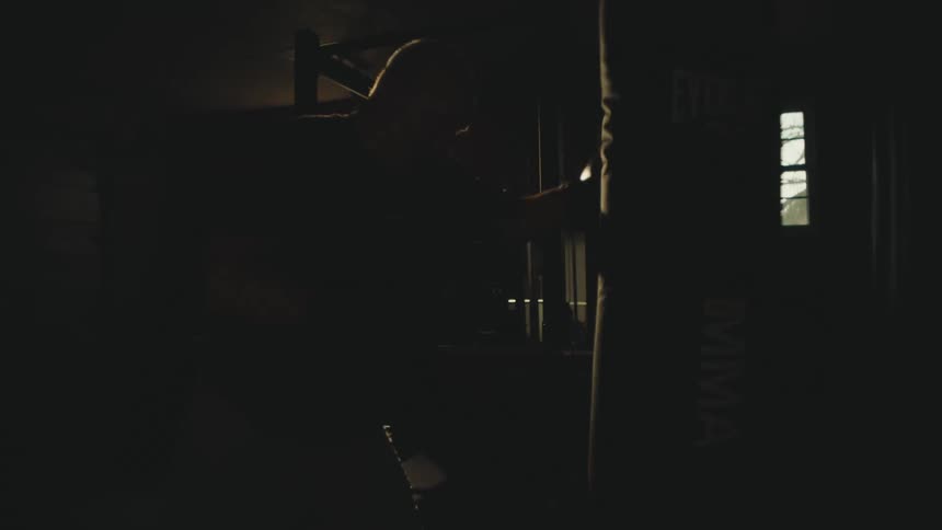 Silhouette of a man throwing punches with boxing gloves on a punching bag in a dark room