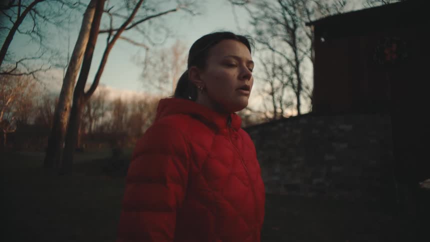 A woman in a red coat looks sad and sighs while standing outdoors