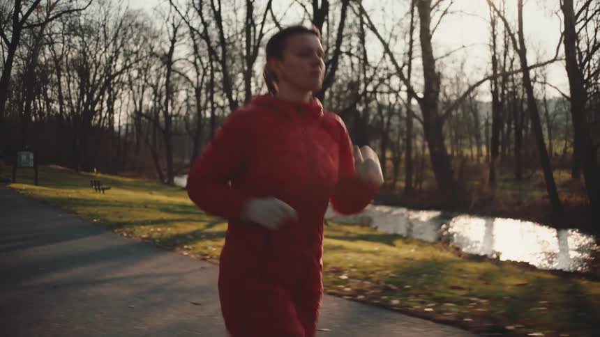 Female runner running in a forest on a path along the river in the morning