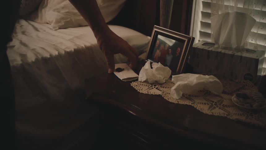 Hand taking a letter from a shelf next to a bed with a picture frame of a family