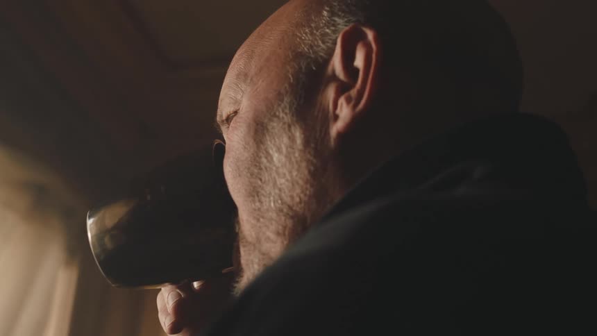 The image depicts a closeup side profile of an individual drinking from a cup in a dimly lit room