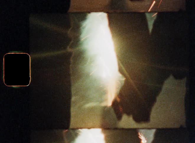 Romantic scene on Super 8 of a man and woman coming together to hold hands while watching fireworks shot and fly into the air or sky and standing on the street at night as a dynamic closeup of their silhouettes